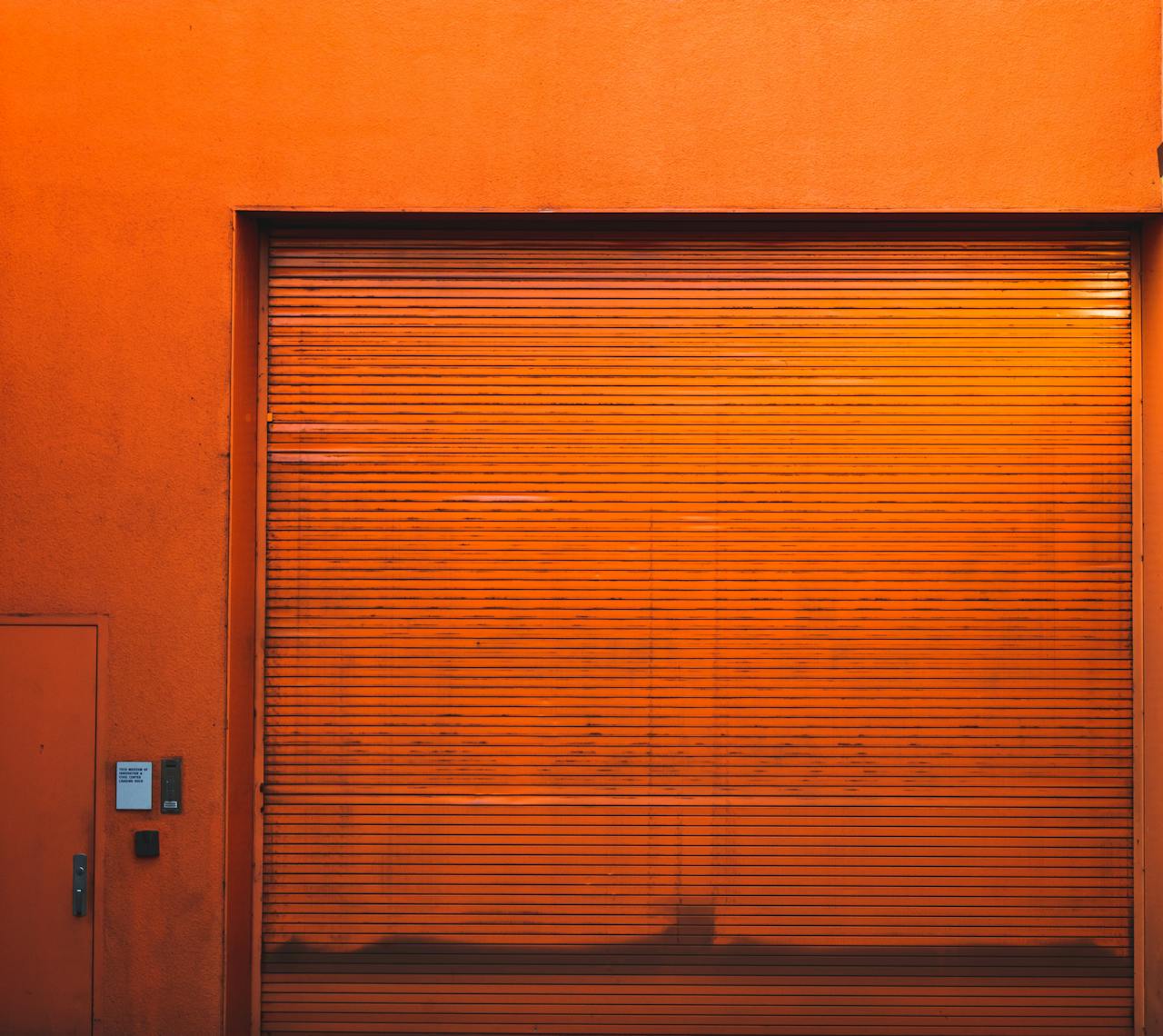 Rustic orange industrial garage door with textured wall creating a vintage urban scene.